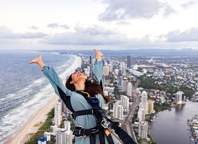 Woman celebrates at the summit of SkyPoint Climb, harnessed and overlooking the coastline—an iconic adrenaline Gold Coast experience with panoramic views.