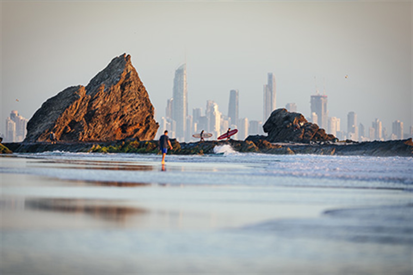 royal-palm-walking-distance-palm-beach Surfers walking the rocks at Currumbin Beach at low tide with the Gold Coast skyline, a short walk from Royal Palm